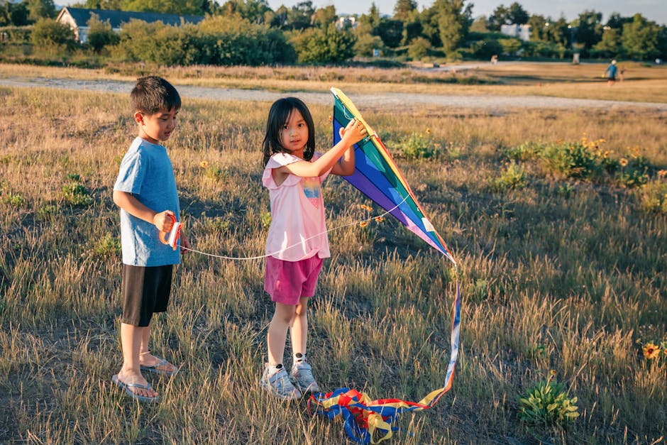 Two children flying a colorful kite in a grassy field, enjoying a sunny day.