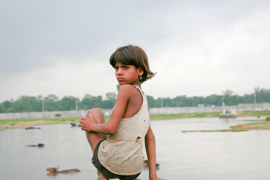 A thoughtful young girl looks over a lake in Jaipur, India, under a cloudy sky.