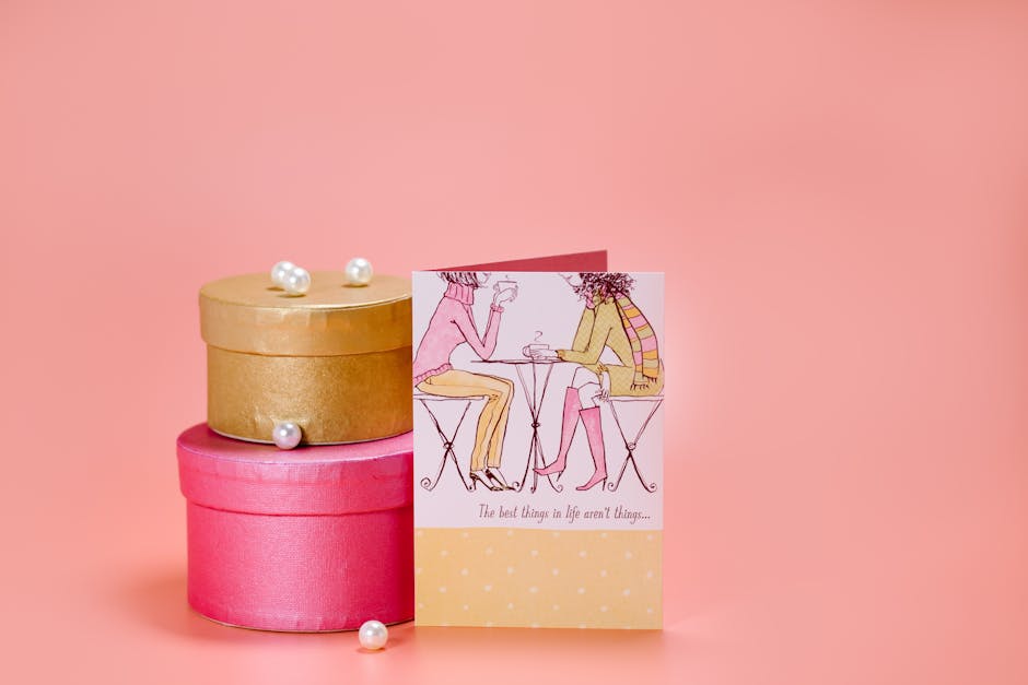 Stacked gift boxes with pearls and a greeting card on a peach background, perfect for celebrations.