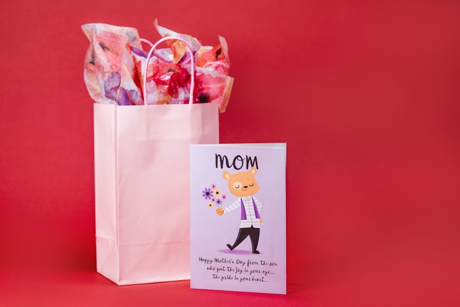 Pink gift bag with colorful tissue paper and Mother's Day card with illustration against red background.