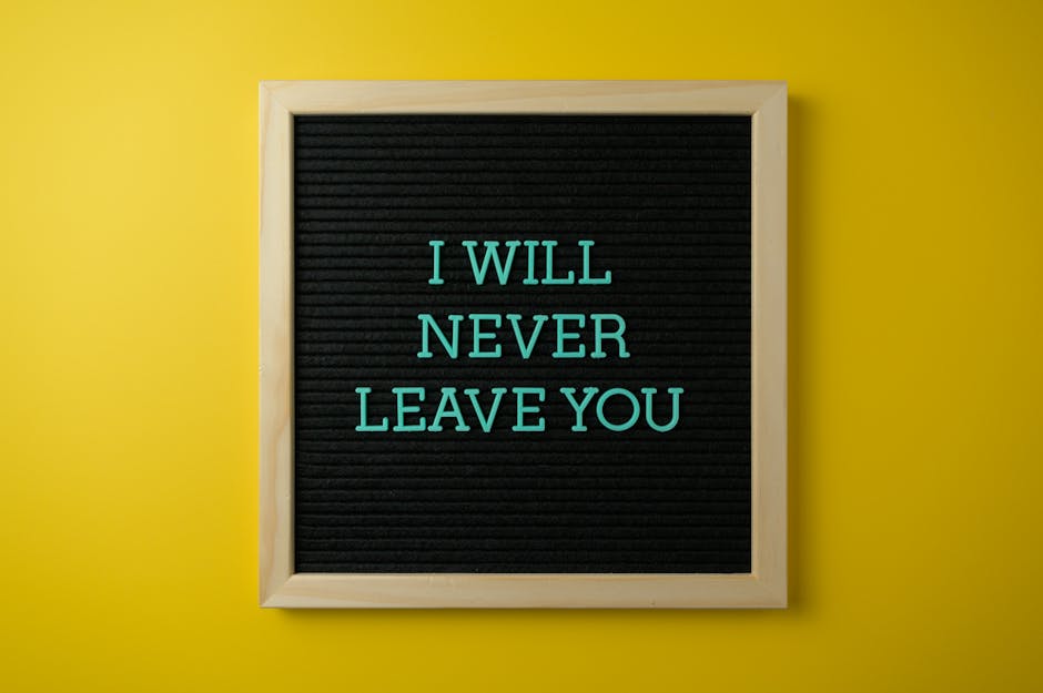 Inspirational quote 'I Will Never Leave You' on a black letter board against a yellow wall.