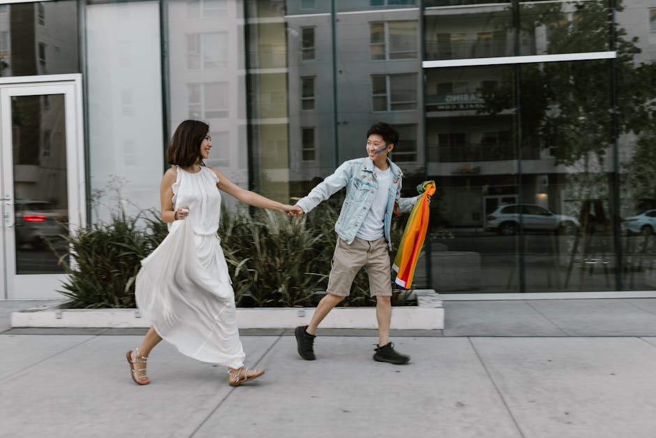 A joyful LGBTQ+ couple holding hands and walking with a rainbow flag in an urban setting.