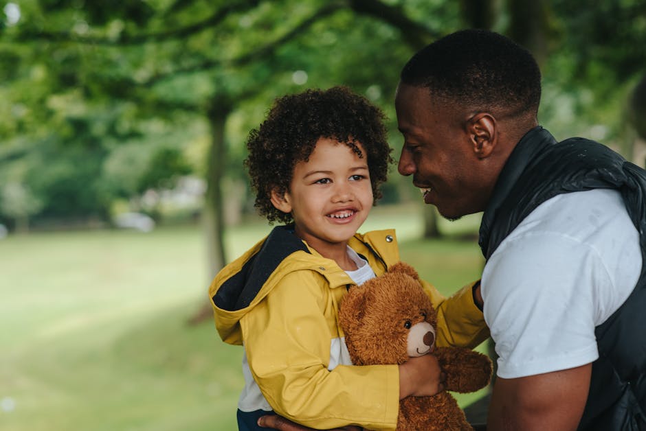 Joyful father and son bonding outdoors, sharing a hug with a teddy bear.