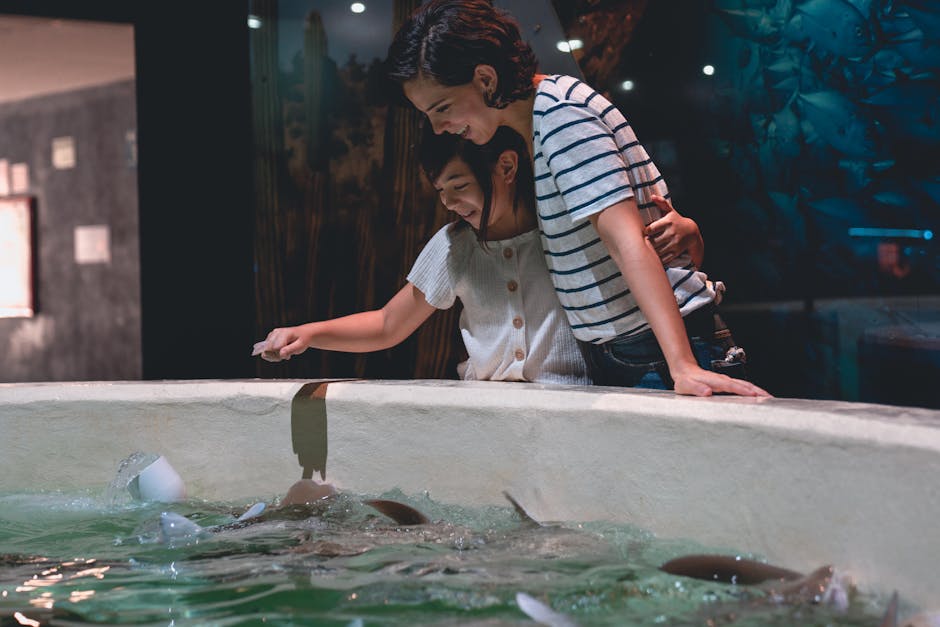 Mother and daughter bonding at an aquarium touch pool, interacting with marine life.