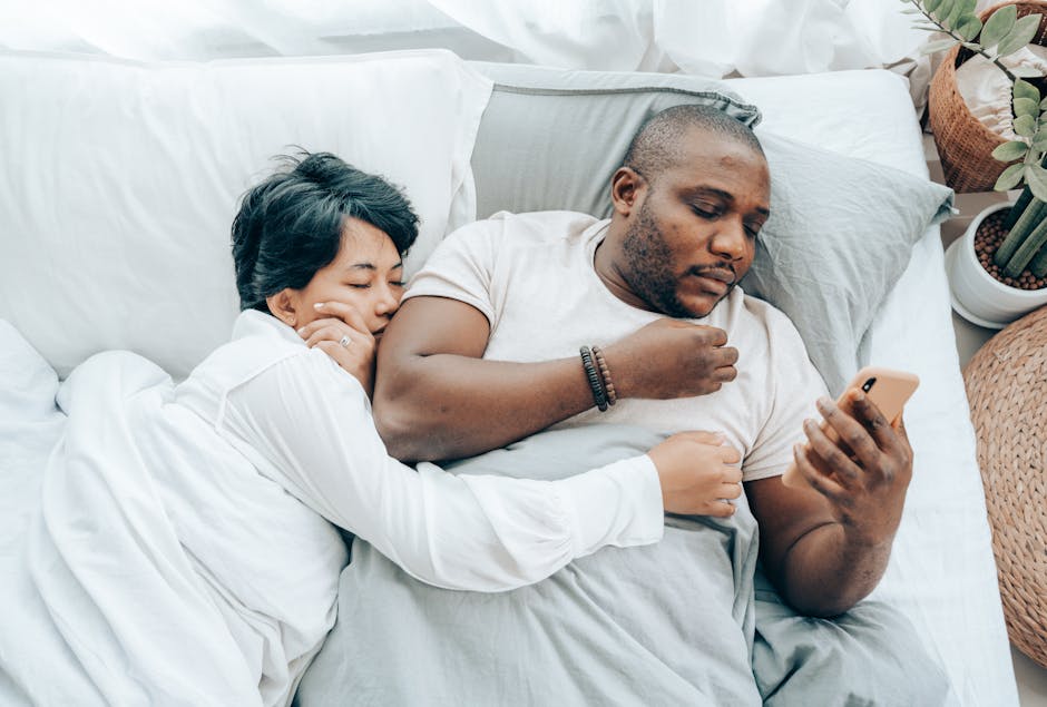 A loving couple cuddling in bed, enjoying a peaceful moment while browsing a smartphone.