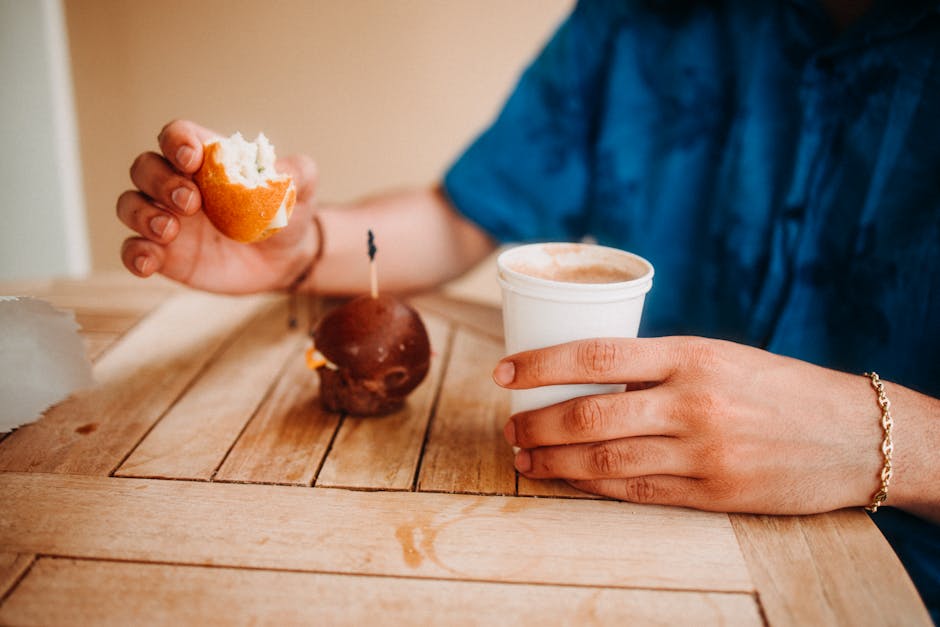 Person enjoying a cozy coffee break with a fresh pastry on a wooden table.