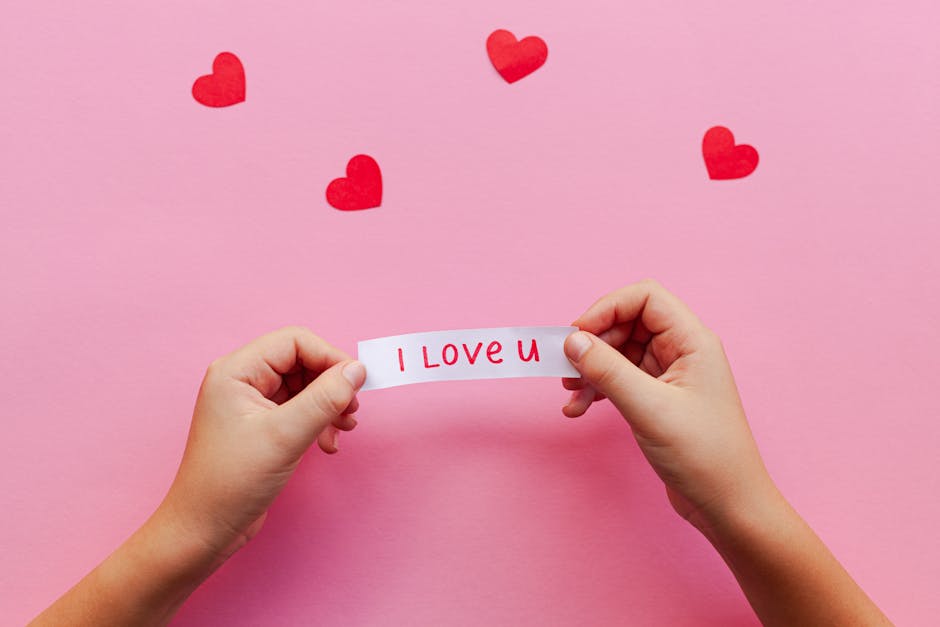 Hands holding an 'I Love U' note on a pink background with red hearts. Perfect for Valentine's themes.