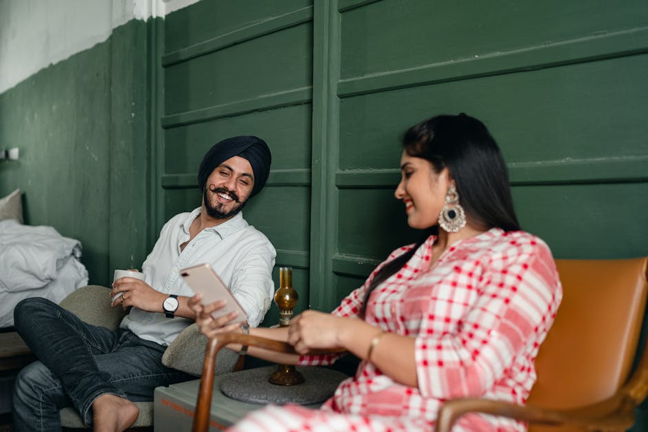 A cheerful couple relaxing indoors, enjoying coffee and smartphone browsing.