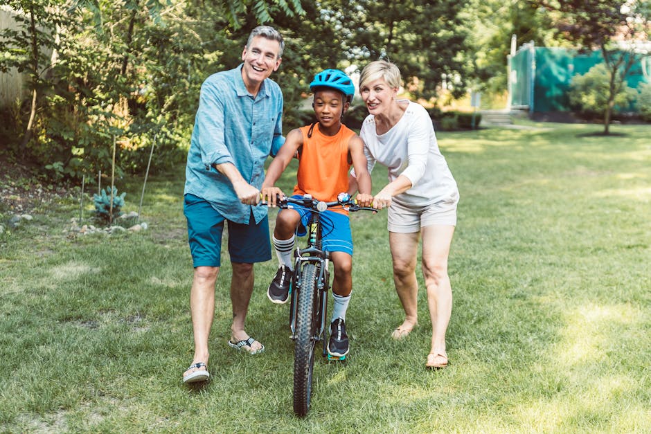 A family helps a young boy learn to ride a bicycle outdoors.