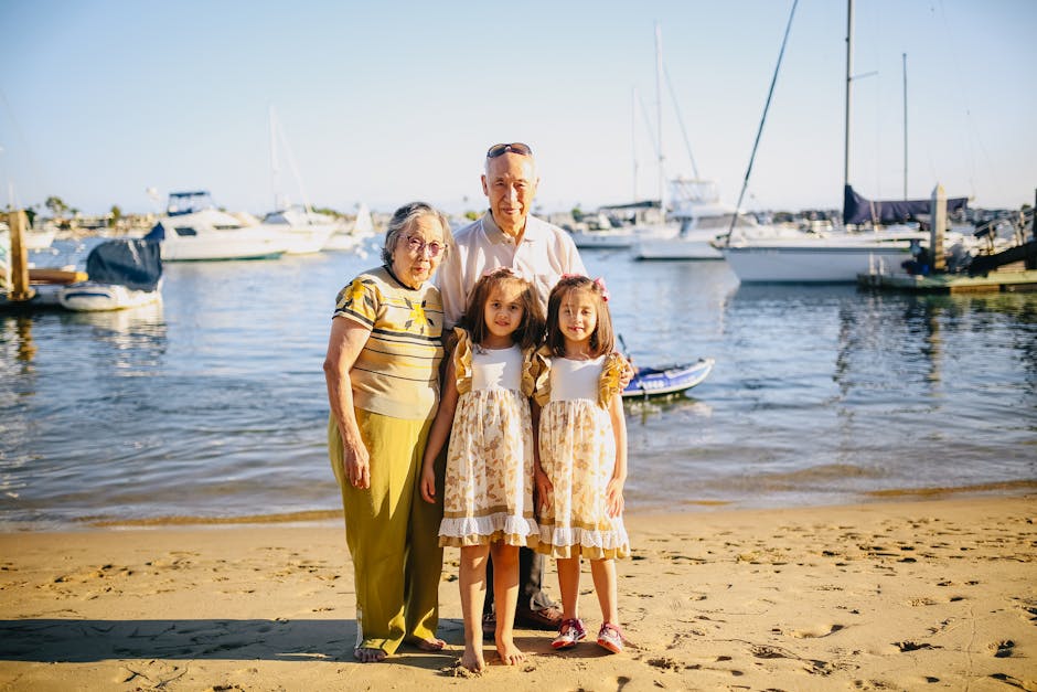 Asian grandparents with twin granddaughters enjoying a sunny beach day.