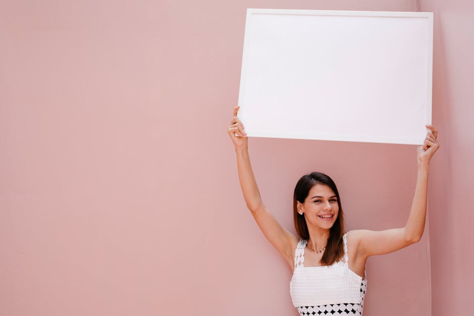 A brunette woman in a white dress holds a blank sign with a pink background, offering ample copy space.