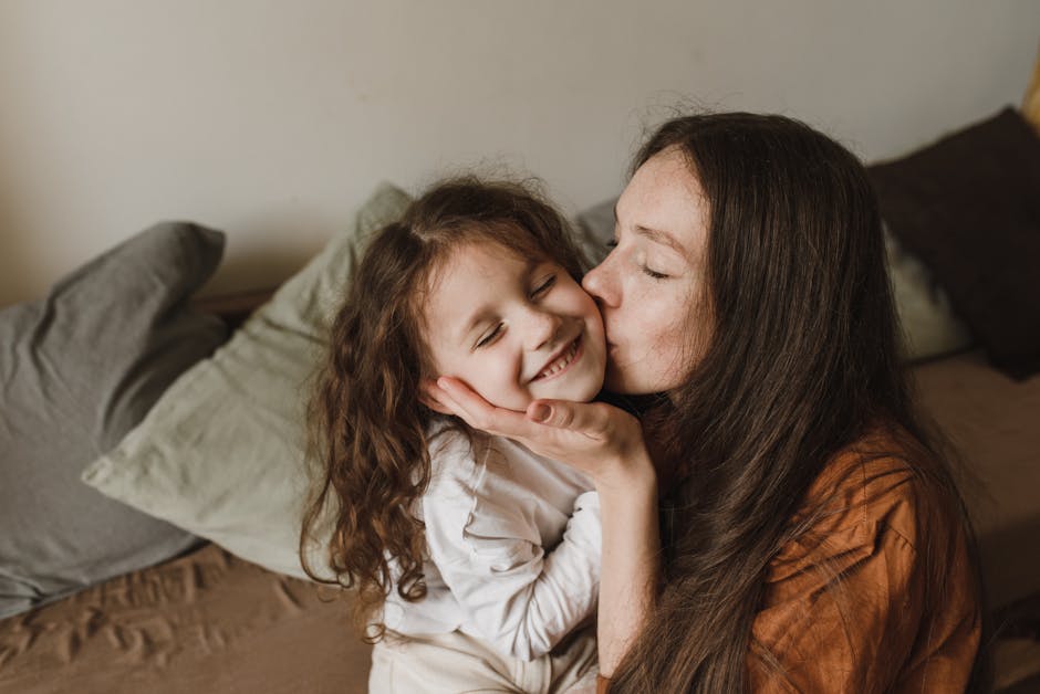 A tender moment of a mother kissing her smiling daughter indoors.