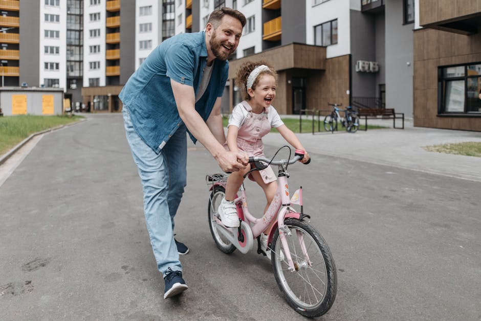 A joyful moment as a father helps his daughter ride a bicycle in an urban setting.