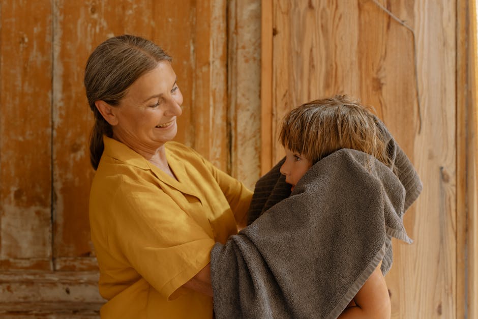 A smiling grandmother tenderly dries her grandson with a towel in a cozy indoor setting.