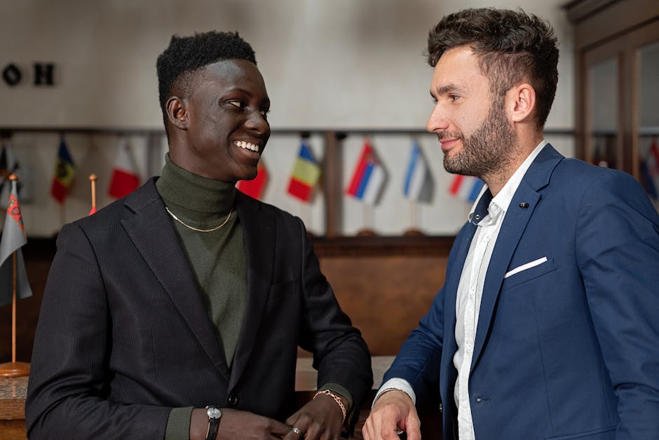 Two smiling businessmen in smart suits engaging in conversation indoors.