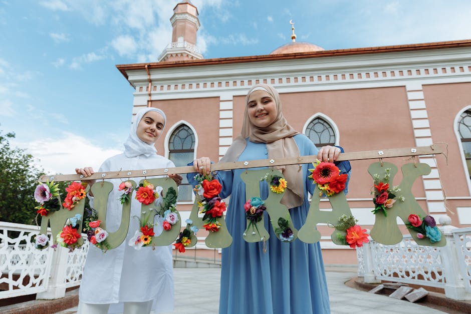 Two joyful Muslim women hold a decorative Eid Mubarak sign near a mosque, celebrating the festive occasion.