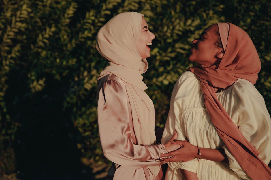 Two women in hijabs enjoying a happy moment in the sunlit outdoors.