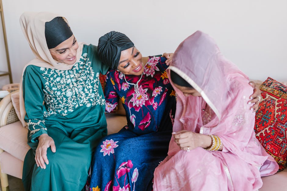 Three Muslim women in colorful attire sharing laughter and togetherness indoors.