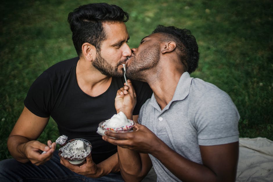 Interracial gay couple sharing an intimate moment with ice cream in a park setting, showcasing love and togetherness.