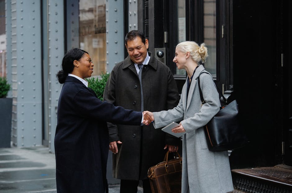 Diverse business professionals engage in a friendly handshake outside an urban building.