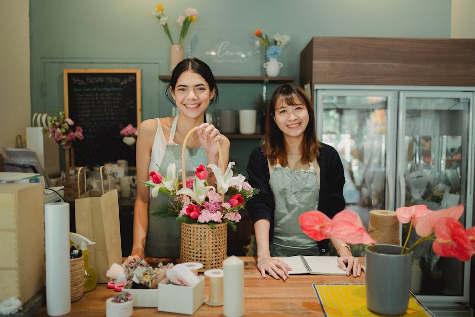 Two female florists smiling in a cozy flower shop, showcasing a vibrant bouquet.
