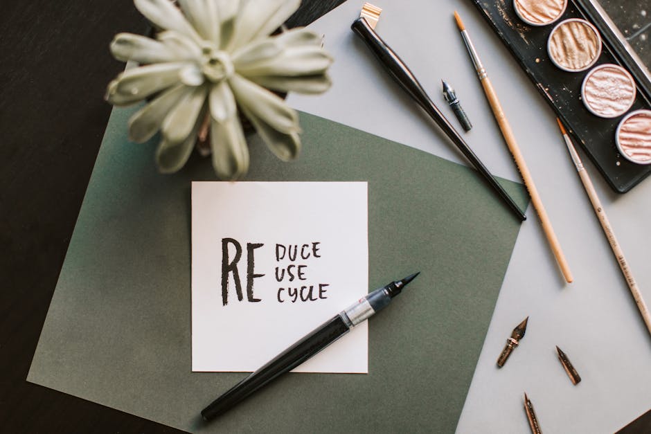 Flat lay of art materials featuring a recycle-themed note and calligraphy tools.