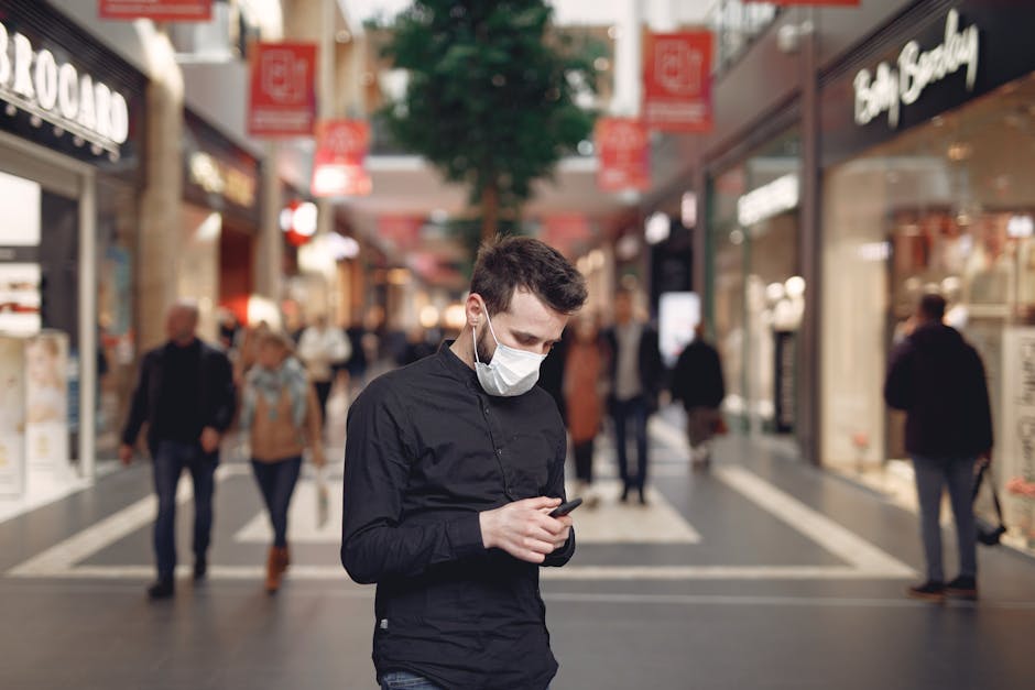 A man in a face mask using his smartphone inside a shopping mall.