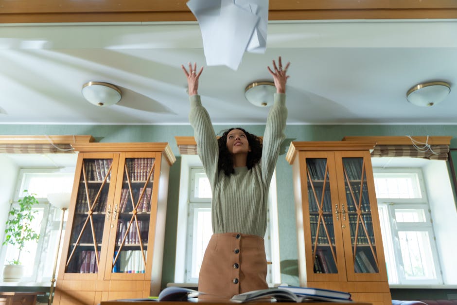A young woman throws papers in the air in a library, expressing joy and relief.