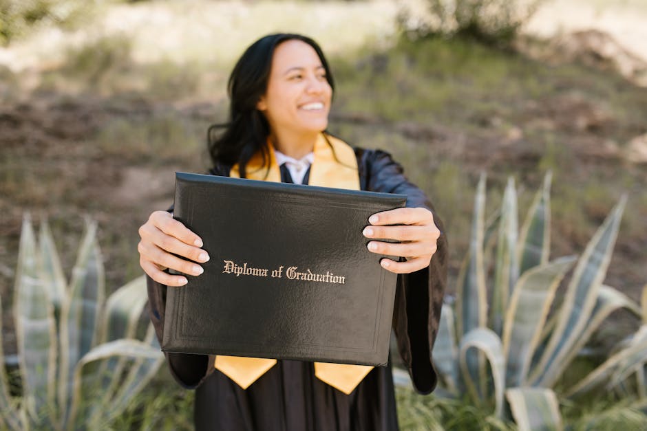 Smiling graduate in cap and gown holding diploma with pride in an outdoor setting.
