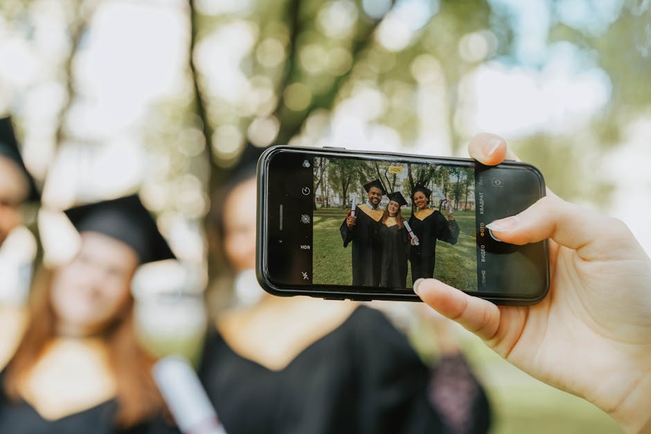 A group of graduates taking a photo with a smartphone in a park setting.