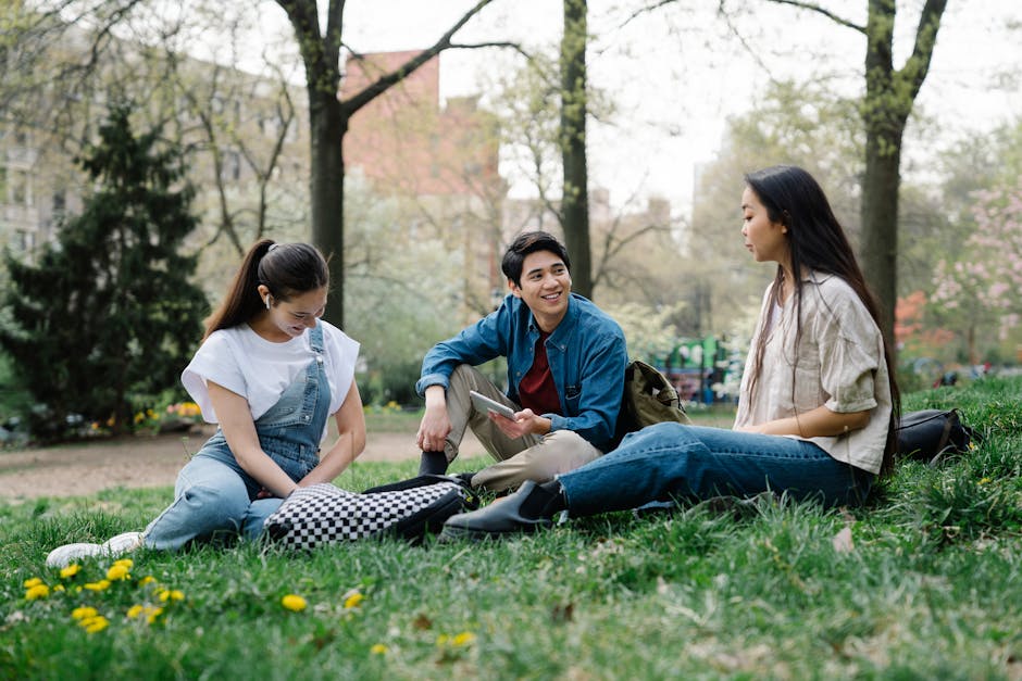 A group of young adults sitting on grass, having a lively conversation in a park setting.