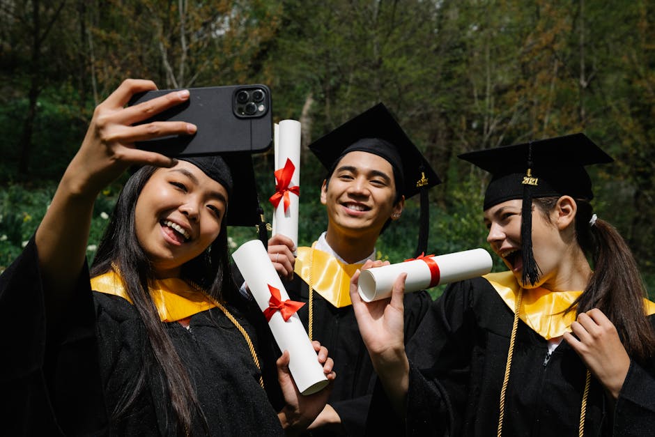 Three young graduates in caps and gowns celebrate by taking a selfie, holding diplomas.