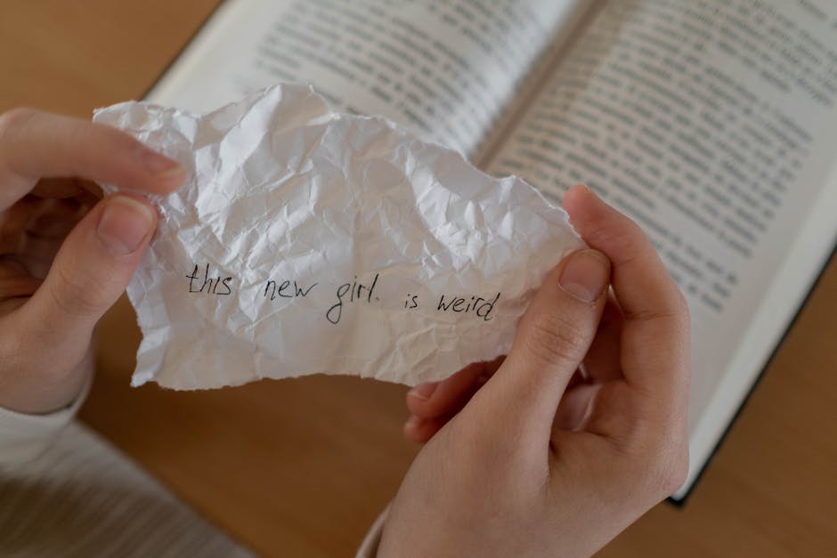 Close-up of hands holding a crumpled note with a handwritten message over an open book.