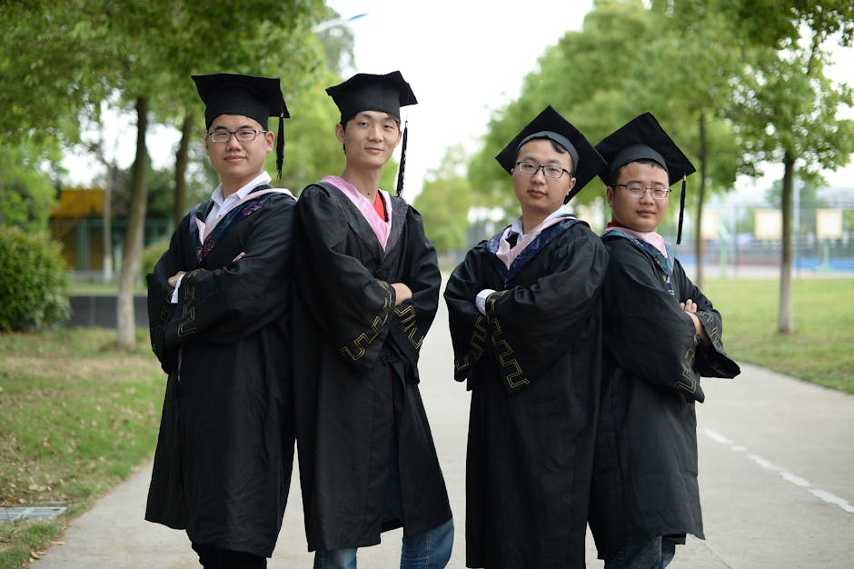 Four male graduates in cap and gown pose outdoors, celebrating achievement.