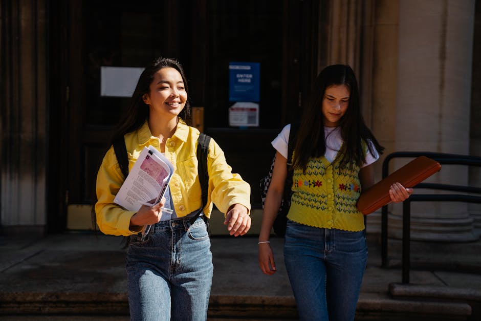 Two college students walking together, smiling and carrying books, on a sunny campus day.