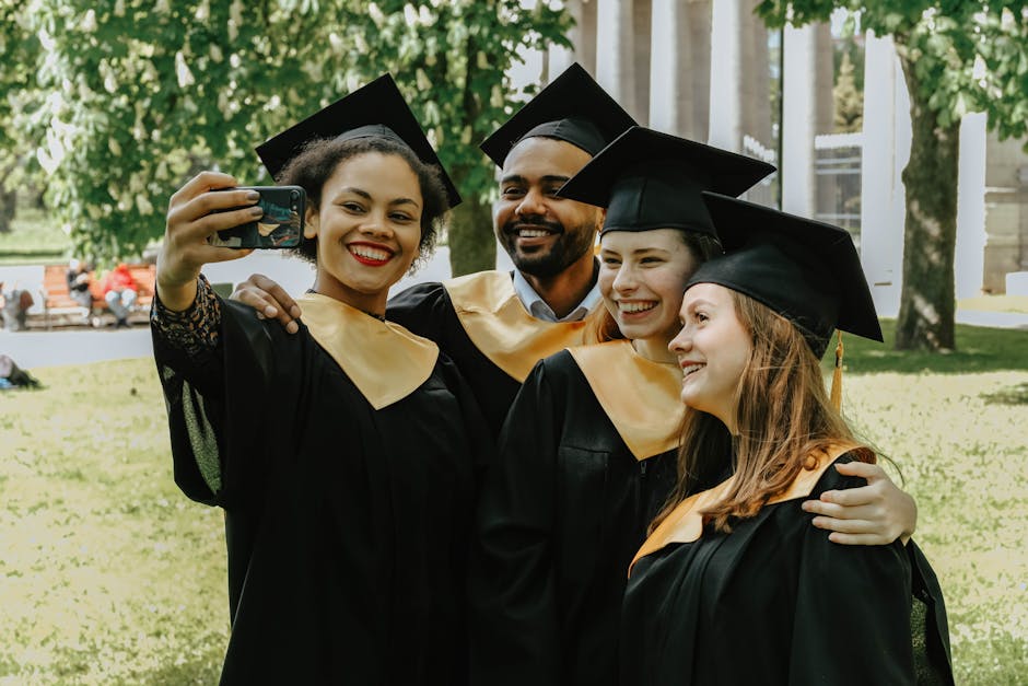 Group of diverse college graduates taking a selfie in their caps and gowns outdoors.