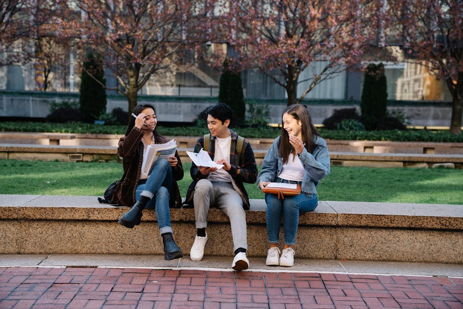 Group of college students laughing and studying outdoors on a campus bench during spring.
