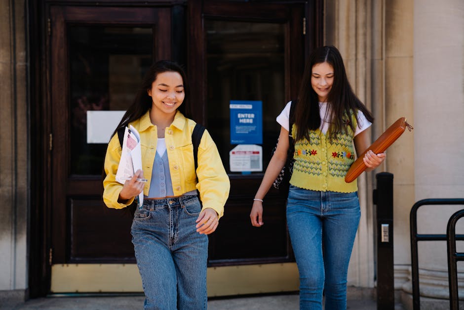 Two young women leaving a university building holding books and smiling.