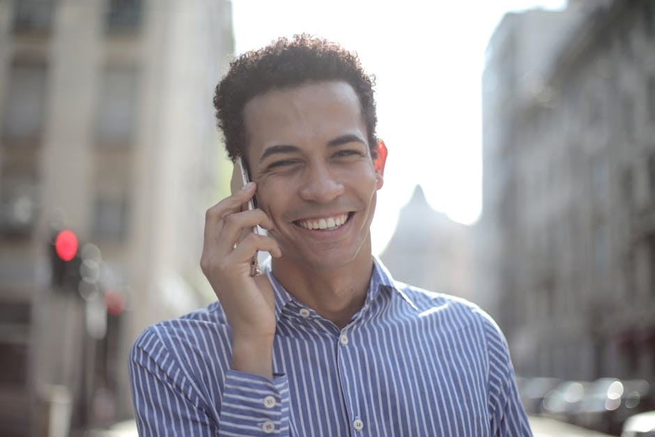 Cheerful young man with curly hair enjoying a phone call in a sunny urban area.
