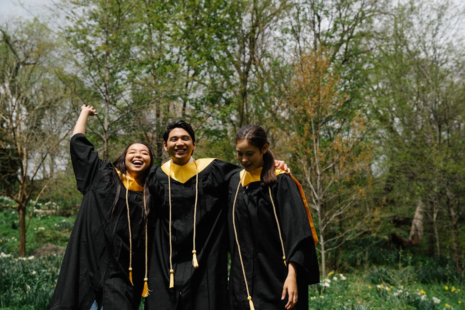Three graduates celebrating their achievement in caps and gowns with vibrant smiles outdoors.