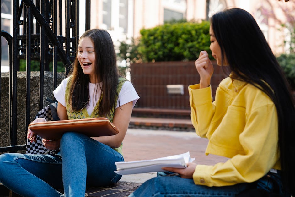 Two young women sit outdoors, studying and enjoying each other's company on a sunny day.