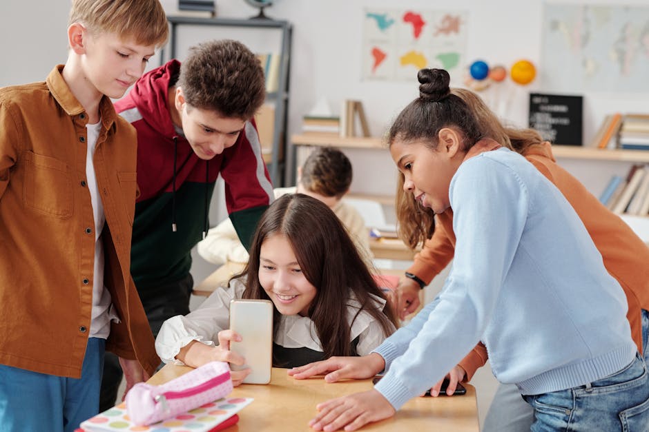 Group of teenagers engaging with a smartphone in a lively classroom environment.