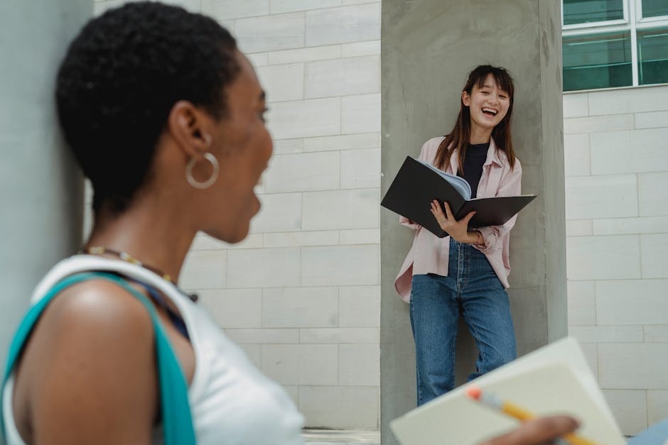 Two female students from different backgrounds sharing a joyful moment while studying outdoors.