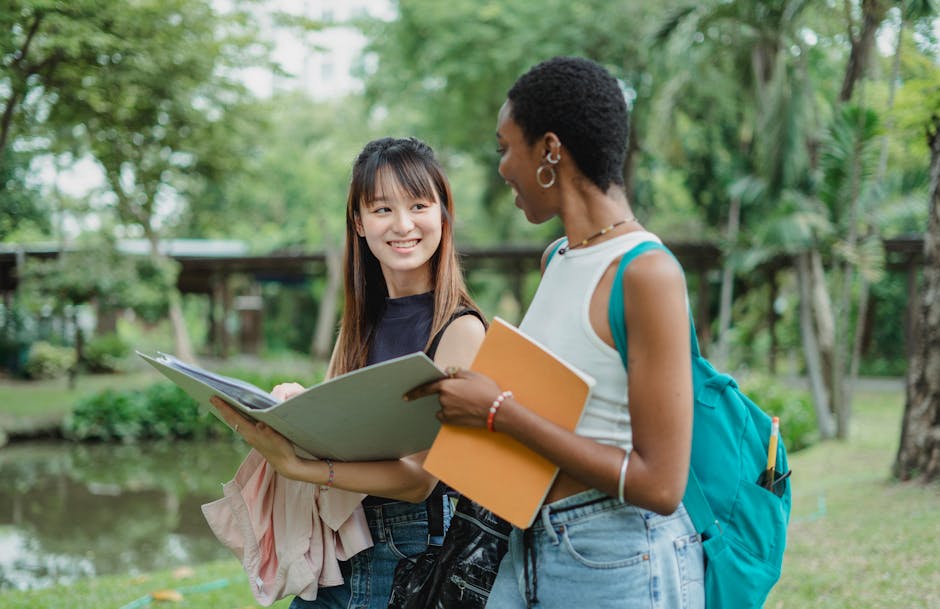 Two diverse college students exchange smiles and ideas outdoors during a sunny day study session.