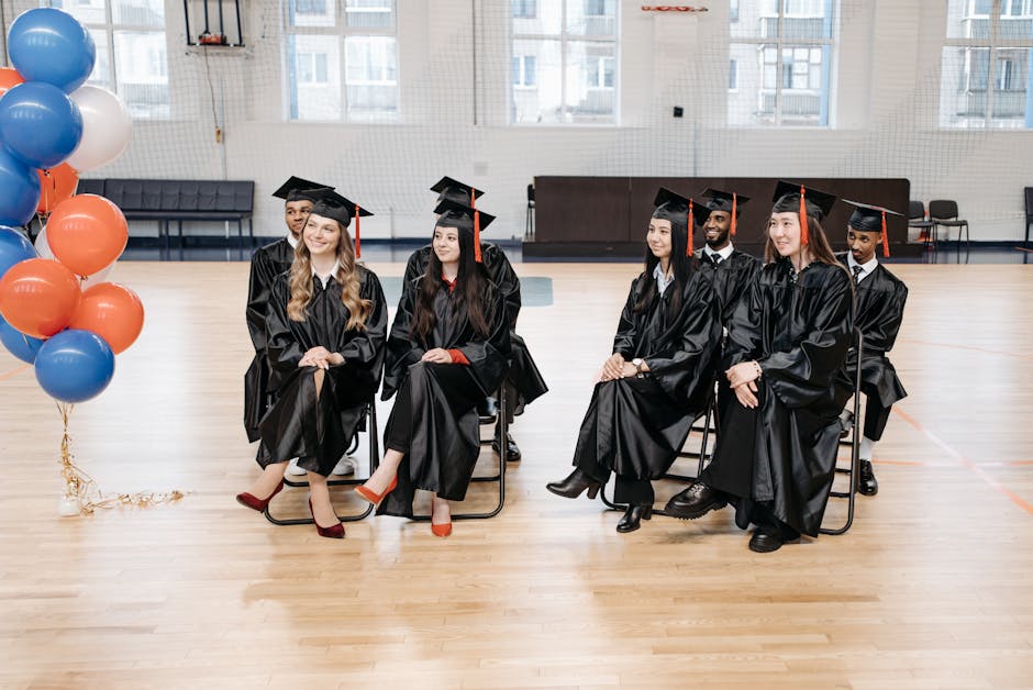 A diverse group of graduates in gowns and caps seated together indoors, celebrating their achievements.