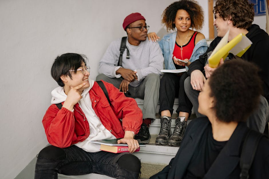 A diverse group of students sitting on stairs, smiling and collaborating indoors.