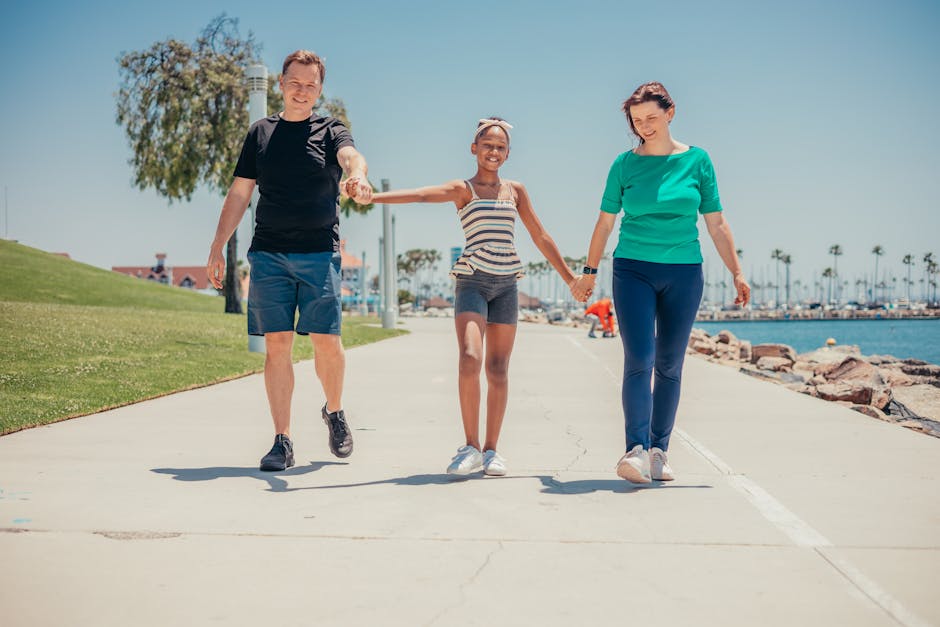 A joyful family of three walking hand-in-hand by the water on a sunny day.