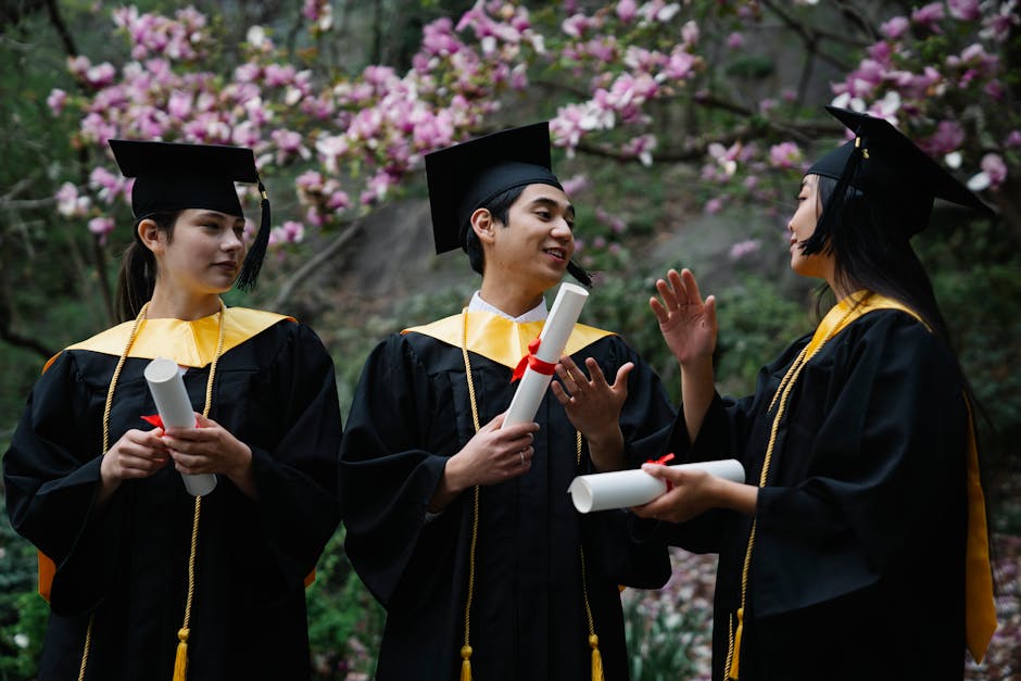 Three graduates in caps and gowns celebrating their success outdoors with diplomas in hand.