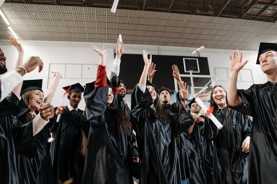 Graduation celebration with diverse students in black gowns throwing caps indoors.