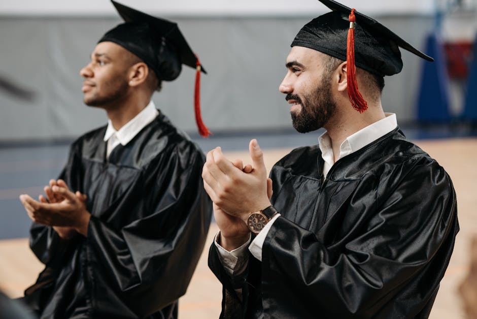 Two graduates clapping and celebrating their achievements in caps and gowns during a graduation ceremony.